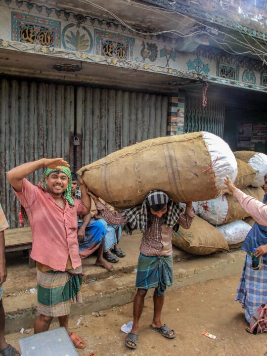 Local posing for a photo, the person on the left side told his friend to lift the heavy bag just for the photo in Bangladesh